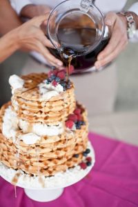 A couple pours syrup onto their waffle wedding cake.